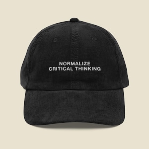 May include: A black corduroy baseball cap featuring the embroidered white text NORMALIZE CRITICAL THINKING centred on the front panel. The hat has a structured crown, a curved brim, and stitched eyelets for ventilation on the top panels.