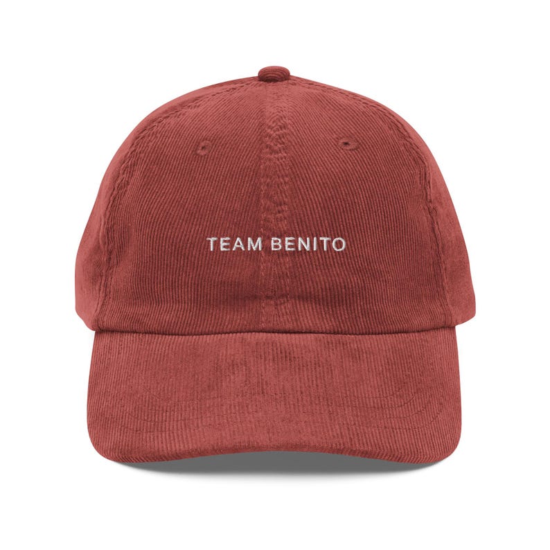 Puede incluir: Gorra de b&eacute;isbol de pana rojo ladrillo con visera curva. El texto "TEAM BENITO" est&aacute; bordado en blanco en la parte delantera. La gorra tiene una corona redondeada y un peque&ntilde;o bot&oacute;n en la parte superior.