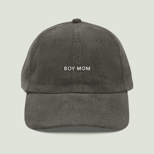 Könnte beinhalten: Eine dunkelgraue Baseballkappe aus Cord mit dem in weißem Garn aufgestickten Text BOY MOM auf der Vorderseite. Die Kappe hat eine strukturierte Krone, einen gebogenen Schirm und einen Knopf oben, was eine durchgehend texturierte Oberfläche zeigt.