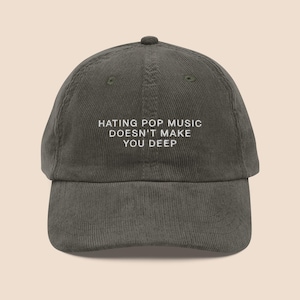 Op de afbeelding: Olijfgroene corduroy baseball cap met de witte tekst: "HATING POP MUSIC DOESN'T MAKE YOU DEEP". De cap heeft een gebogen klep en een ronde kroon. Een casual accessoire voor dagelijks gebruik.