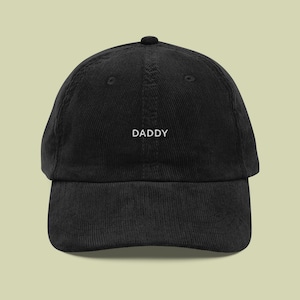 Peut inclure: Casquette de baseball noire en velours côtelé avec le mot "DADDY" brodé en blanc. La casquette a une visière incurvée et une couronne structurée. Un accessoire décontracté classique.