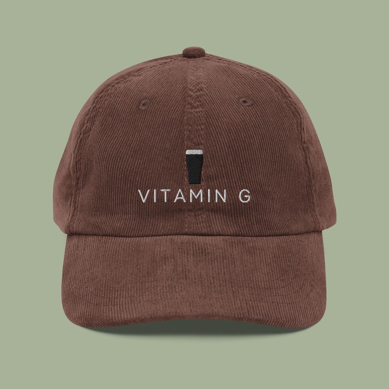 Op de afbeelding: Een bruine corduroy baseballpet met een wit geborduurd ontwerp van een pintglas en de tekst "VITAMIN G".