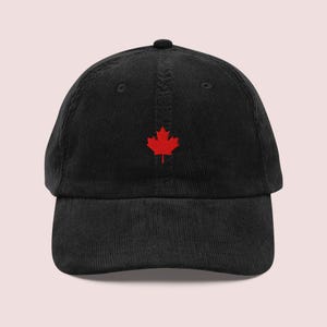 Op de afbeelding: Zwarte corduroy baseballcap met een rood geborduurd esdoornblad. De cap heeft een gebogen klep en een gestructureerde kroon. Een klassiek, casual accessoire.