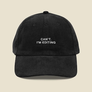 Puede incluir: Una gorra de béisbol de pana negra con el texto bordado en blanco CAN'T. I'M EDITING centrado en el panel frontal. La gorra tiene una corona estructurada, una visera curva y un botón en la parte superior con un acabado de tela texturizada.