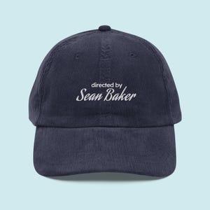 May include: A navy blue corduroy baseball cap with white embroidery that reads "directed by Sean Baker".