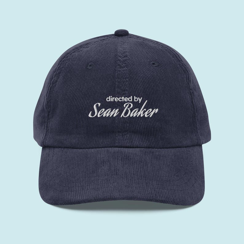 May include: A navy blue corduroy baseball cap with white embroidery that reads "directed by Sean Baker".