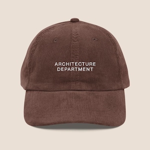 Può includere: Un cappellino da baseball in velluto a coste marrone con il testo ricamato in bianco ARCHITECTURE DEPARTMENT centrato sul pannello frontale. Il cappellino presenta una corona strutturata, una visiera curva e un bottone sulla parte superiore.