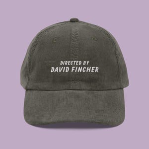 Könnte beinhalten: Eine dunkelgrüne Baseballkappe aus Cord mit weiß gesticktem Text, der "DIRECTED BY DAVID FINCHER" lautet.