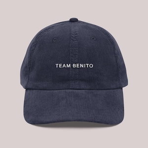 Puede incluir: Gorra de b&eacute;isbol de pana azul marino con el texto "TEAM BENITO" bordado en blanco. La gorra tiene una visera curva y una parte superior redondeada.