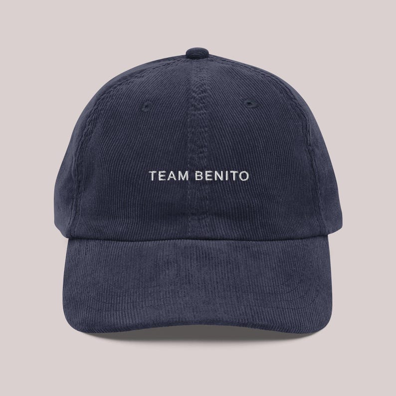 Puede incluir: Gorra de b&eacute;isbol de pana azul marino con el texto "TEAM BENITO" bordado en blanco. La gorra tiene una visera curva y una parte superior redondeada.