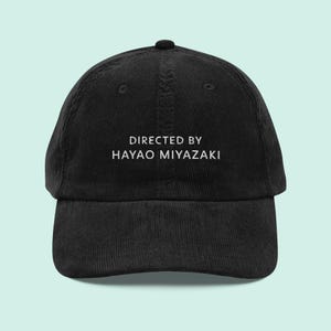 May include: Black corduroy baseball cap with white text that reads "Directed by Hayao Miyazaki".