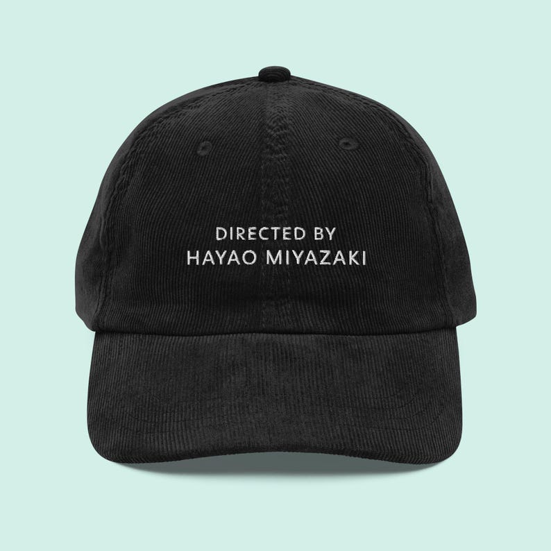 May include: Black corduroy baseball cap with white text that reads "Directed by Hayao Miyazaki".
