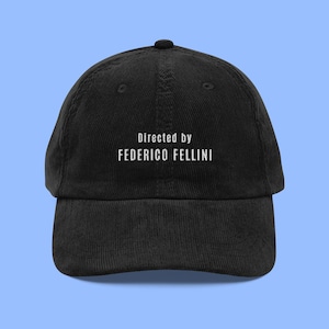 May include: Black corduroy baseball cap with white embroidered text that reads "Directed by FEDERICO FELLINI".