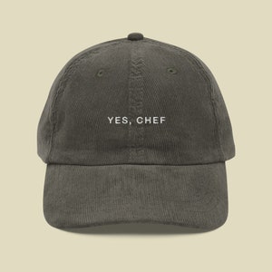 May include: A dark gray corduroy baseball cap with the text "YES, CHEF" embroidered in white on the front.