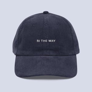 Peut inclure: Casquette de baseball en velours côtelé bleu marine avec le texte "BI THE WAY" brodé en blanc. La casquette a une visière incurvée et une couronne arrondie. Un accessoire décontracté.