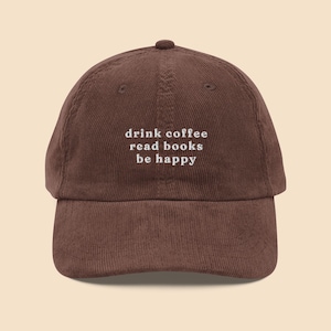 Puede incluir: Una gorra de béisbol de pana marrón con el texto "drink coffee read books be happy" bordado en blanco.