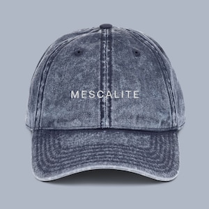 Pode incluir: Boné de beisebol em ganga azul desbotado com a palavra "MESCALITE" bordada em branco. O boné tem uma viseira curva e uma alça ajustável. Um acessório de moda casual.