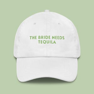 May include: White baseball cap with green text that reads "The Bride Needs Tequila".