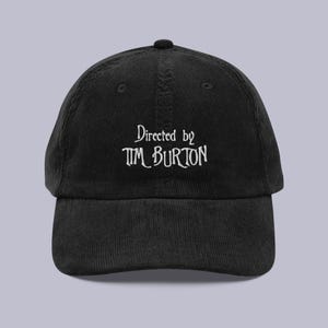 May include: Black corduroy baseball cap with the text "Directed by Tim Burton" embroidered in white. The cap has a curved brim and an adjustable strap at the back. A stylish accessory for fans of the director.