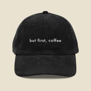 Puede incluir: Una gorra de béisbol de pana negra con el texto bordado en blanco but first, coffee centrado en el panel frontal. La gorra tiene una corona estructurada, una visera curva y un botón en la parte superior, con un diseño de seis paneles.
