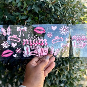 May include: A clear sheet with pink and white stickers featuring butterflies, bows, lips, hearts, and flowers. The text "basic mom" is written in pink script. The stickers have a checkered pattern.