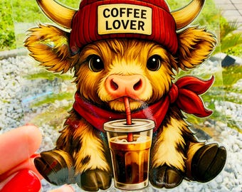 Puede incluir: Una pegatina transparente con un ternero de las Highlands marrón y esponjoso que lleva un gorro rojo con el texto COFFEE LOVER y una bufanda roja. El ternero bebe café helado de un vaso de plástico transparente con una pajita roja.
