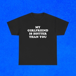 Pu&ograve; includere: T-shirt nero con la scritta bianca "MY GIRLFRIEND IS HOTTER THAN YOU". La maglietta ha girocollo e maniche corte. Lo sfondo &egrave; di colore blu.