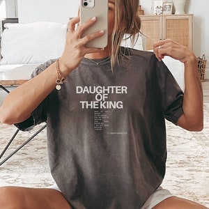 May include: A grey t-shirt with the text "Daughter of the King" and a Bible verse, 2 Corinthians 6:18, printed on the front.
