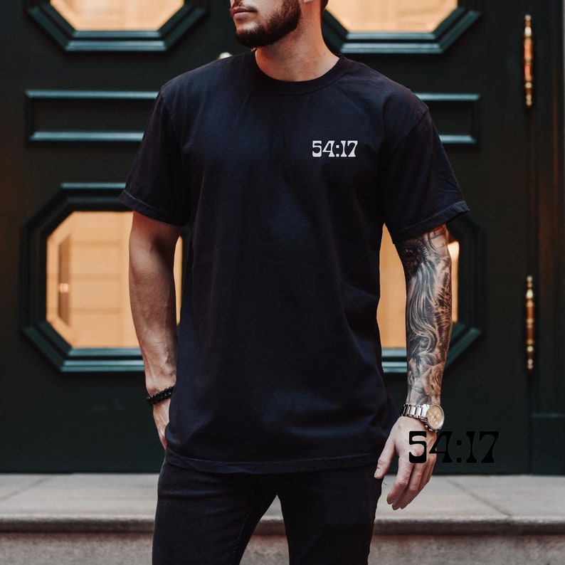 Pode incluir: Uma camiseta preta com o texto "54:17" impresso em branco na frente.