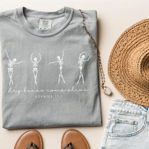May include: Gray t-shirt with a white graphic of four skeletons dancing with the text "dry bones come alive" and "EZEKIEL 37:5" below.
