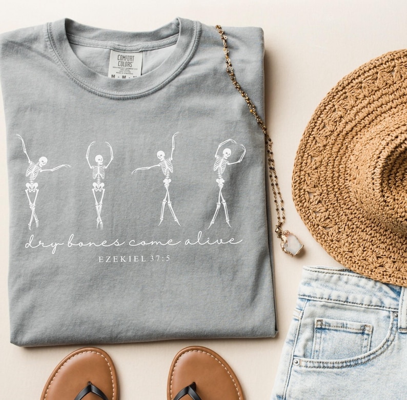 May include: Gray t-shirt with a white graphic of four skeletons dancing with the text "dry bones come alive" and "EZEKIEL 37:5" below.