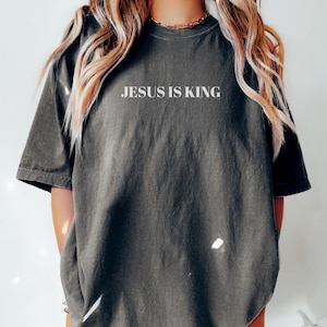 K&ouml;nnte beinhalten: Ein &uuml;berdimensioniertes T-Shirt in dunkelgrau mit dem Aufdruck "JESUS IS KING" in wei&szlig; auf der Vorderseite.