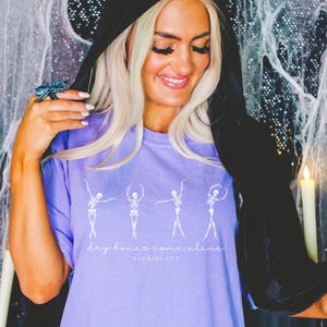 May include: Purple t-shirt with a white graphic of dancing skeletons and the text "Dry bones come alive" with the word "Spooktacular" underneath.