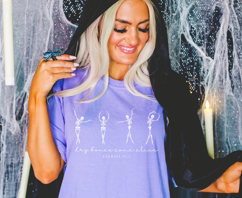 May include: Purple t-shirt with a white graphic of dancing skeletons and the text "Dry bones come alive" with the word "Spooktacular" underneath.