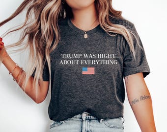 Può includere: Una maglietta grigia scura con il testo "TRUMP WAS RIGHT ABOUT EVERYTHING" in lettere bianche. Una piccola bandiera americana è stampata sotto il testo.