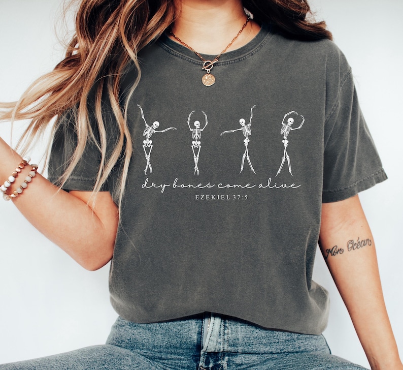 May include: A gray t-shirt with a graphic of five skeletons dancing. The text "dry bones come alive" and "Ezekiel 37:5" is printed below the skeletons.