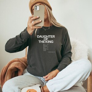 May include: A dark grey long-sleeved sweatshirt with the text "Daughter of the King" and a Bible verse printed in white.
