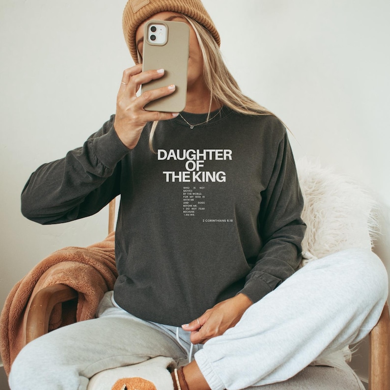 May include: A dark grey long-sleeved sweatshirt with the text "Daughter of the King" and a Bible verse printed in white.