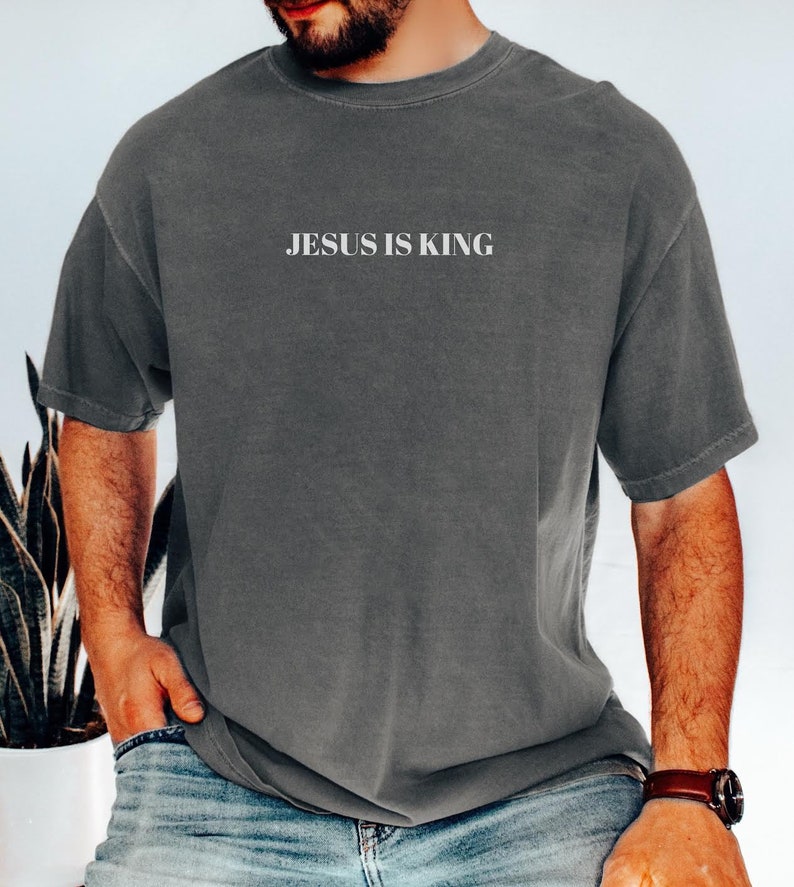 K&ouml;nnte beinhalten: Ein anthrazitfarbenes T-Shirt mit dem Aufdruck "JESUS IS KING" in Wei&szlig; auf der Vorderseite.