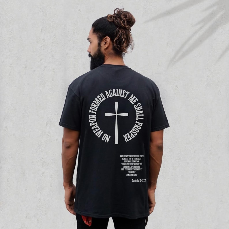 Pode incluir: Camiseta preta com um gr&aacute;fico circular branco nas costas. O gr&aacute;fico apresenta uma cruz e o texto "No weapon formed against me shall prosper." O texto "And every tongue which riseth against thee in judgment thou shalt condemn. This is the heritage of the servants of the Lord, and their righteousness is of me, saith the Lord." est&aacute; impresso abaixo do gr&aacute;fico. O texto "Isaiah 54:17" est&aacute; impresso abaixo da cita&ccedil;&atilde;o.