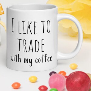 May include: White ceramic coffee mug with black text that reads "I like to trade with my coffee".