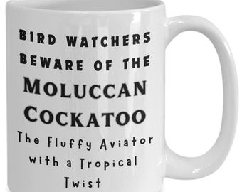 Puede incluir: Taza de café de cerámica blanca con texto negro que dice "Bird Watchers Beware of the Moluccan Cockatoo The Fluffy Aviator with a Tropical Twist"