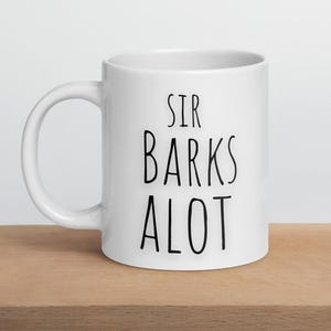 以下が含まれることがあります： 白いセラミック製のマグカップに、黒い文字で「Sir Barks Alot」と書かれています。