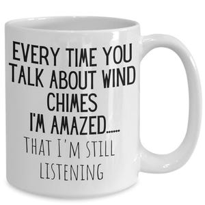 Peut inclure: Mug en céramique blanche avec une anse incurvée. Le mug présente un texte noir qui se lit : "EVERY TIME YOU TALK ABOUT WIND CHIMES I'M AMAZED...... THAT I'M STILL LISTENING."