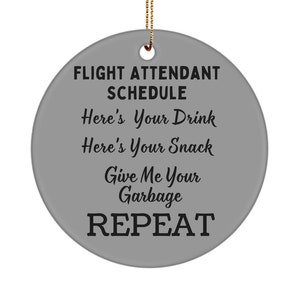 Op de afbeelding: Een ronde grijze ornament met de tekst "FLIGHT ATTENDANT SCHEDULE" en de volgende tekst in een cursief schrift: "Here's Your Drink, Here's Your Snack, Give Me Your Garbage, REPEAT".