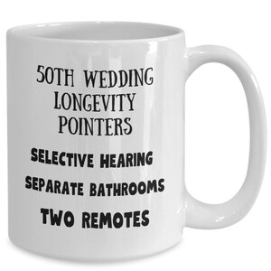 May include: White ceramic coffee mug with black text that reads "50th Wedding Longevity Pointers: Selective Hearing, Separate Bathrooms, Two Remotes".