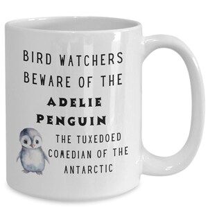 Peut inclure: Une tasse à café en céramique blanche avec une illustration en noir et blanc d'un manchot Adélie. La tasse porte l'inscription "Bird Watchers Beware of the Adelie Penguin The Tuxedoed Comedian of the Antarctic."
