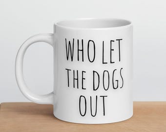 May include: White ceramic coffee mug with black text that reads "Who Let The Dogs Out".
