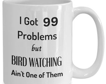 Puede incluir: Taza de café de cerámica blanca con texto negro que dice "Tengo 99 problemas, pero observar pájaros no es uno de ellos".