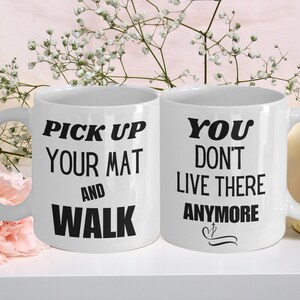 Puede incluir: Dos tazas de café blancas con texto negro. La taza de la izquierda dice "Pick up your mat and walk". La taza de la derecha dice "You don't live there anymore".